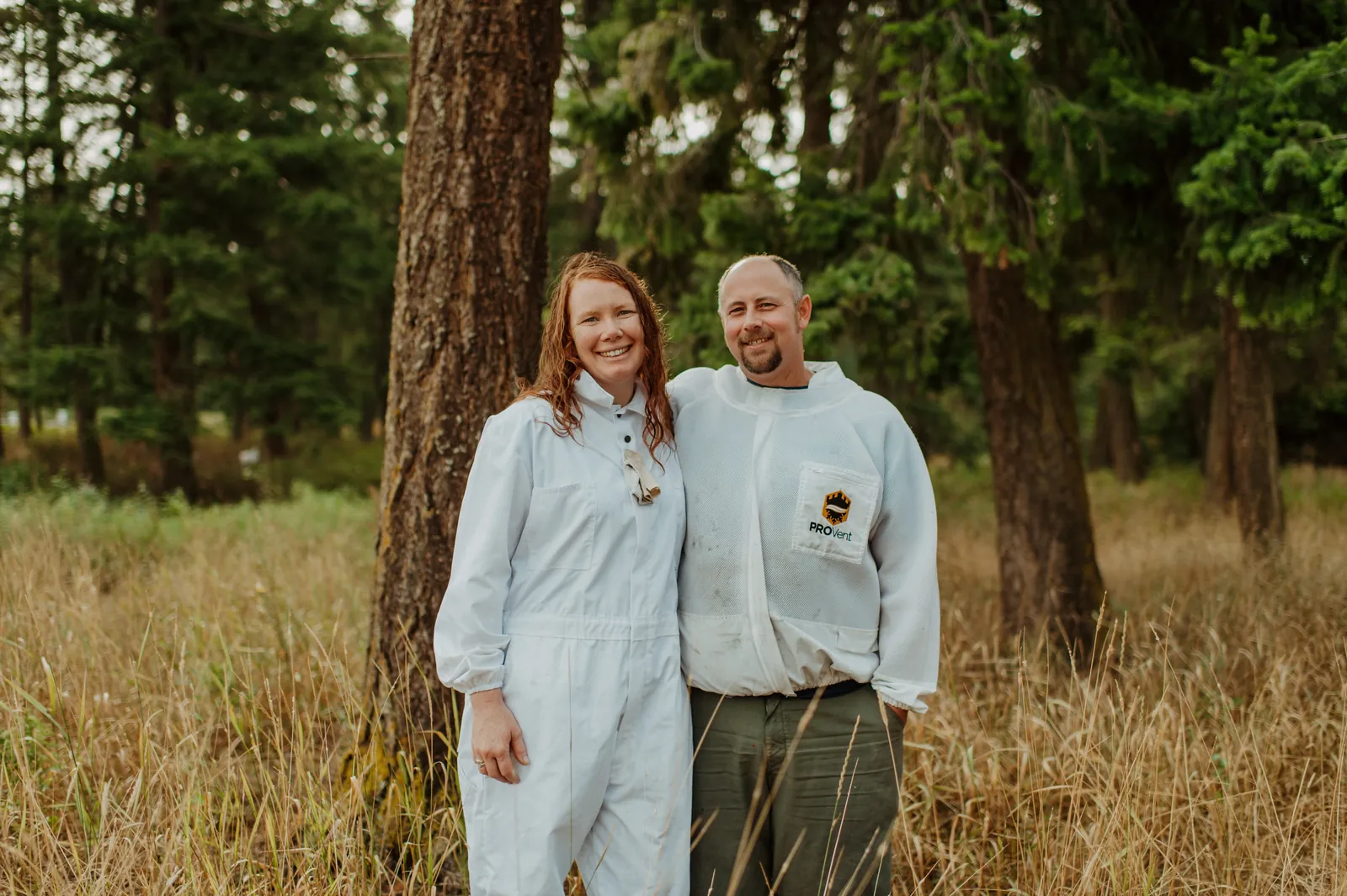 Emily and Shayne in bee suits among the pines on the farm.