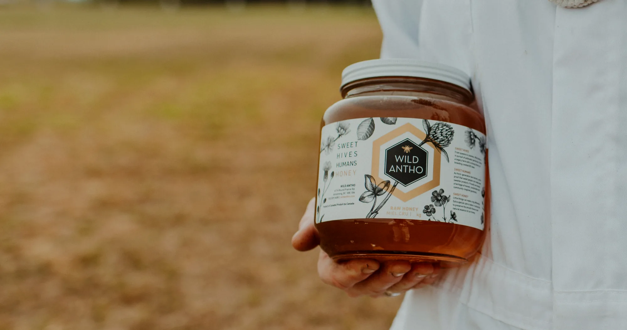 A beekeeper holding a jar of Wild Antho honey in the field.